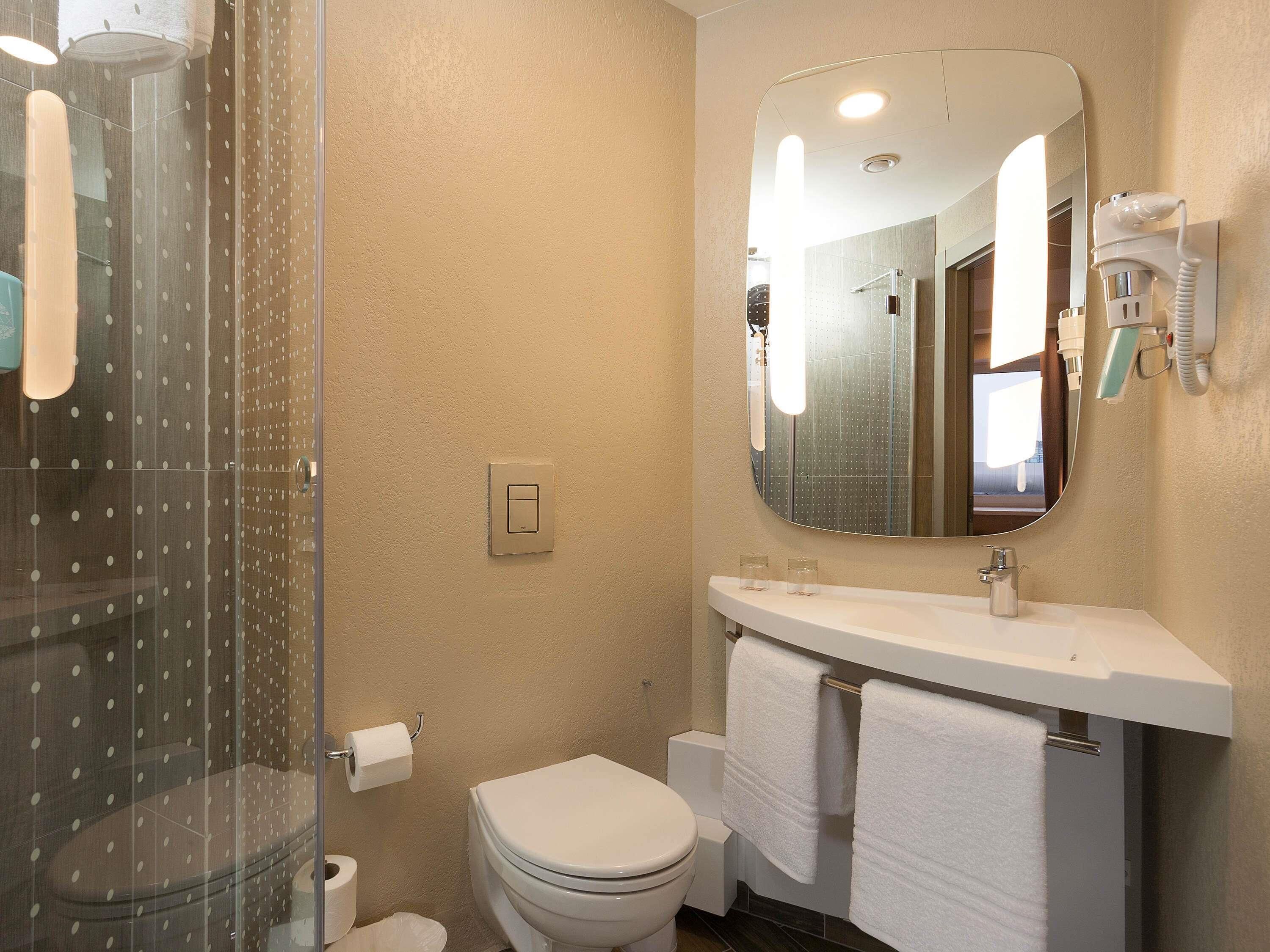 Un baño con cabina de ducha de vidrio, un inodoro, un lavabo con espejo y un perchero para toallas.