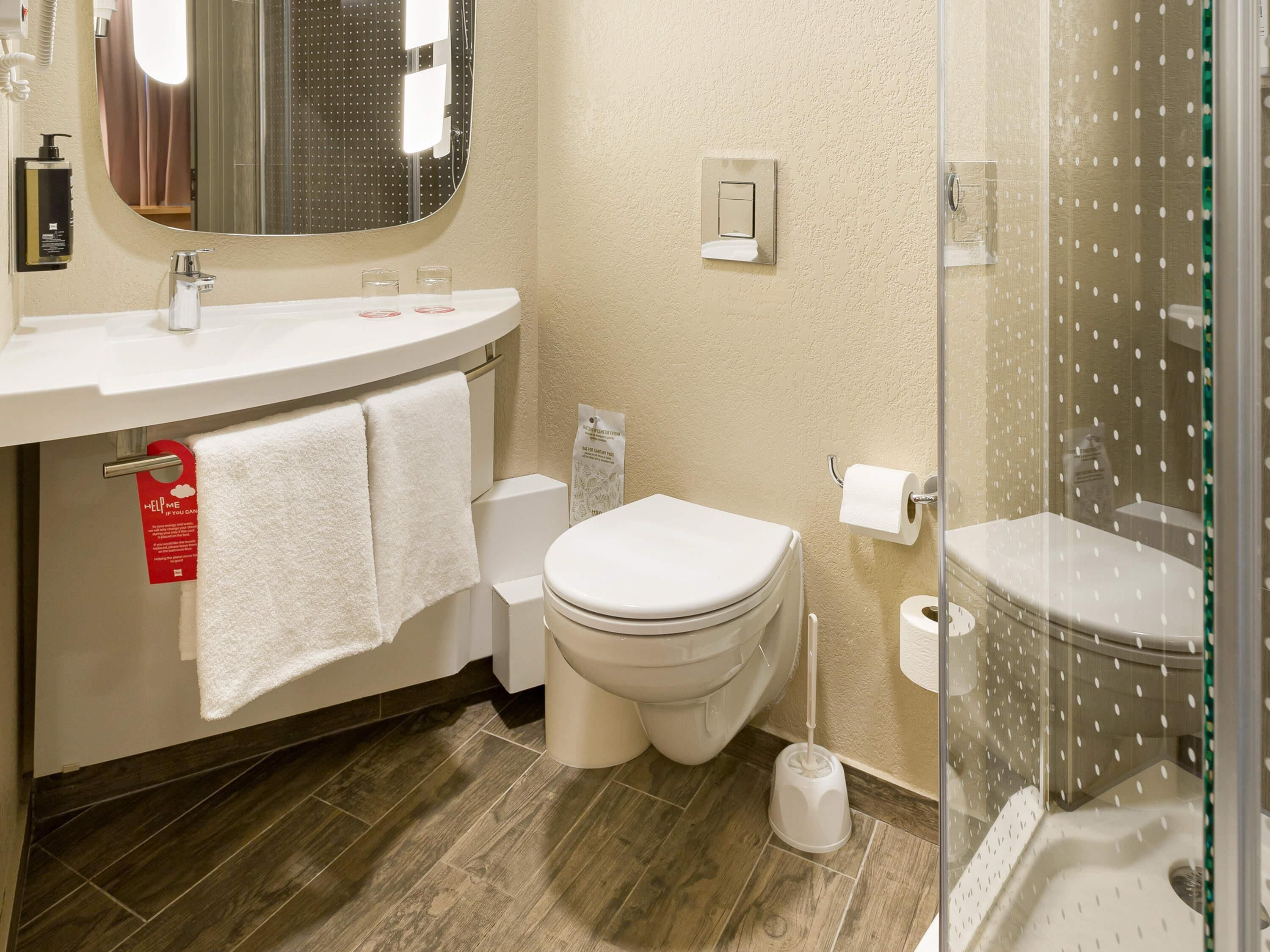A bathroom with a toilet, bidet, and shower. There are towels hanging on a rack, a soap dispenser, and a toilet paper holder.