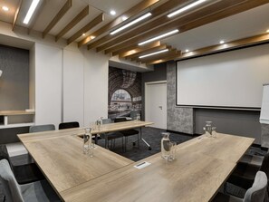Een congreszaal met houten tafels, stoelen, een projectiescherm en een groot raam met uitzicht.