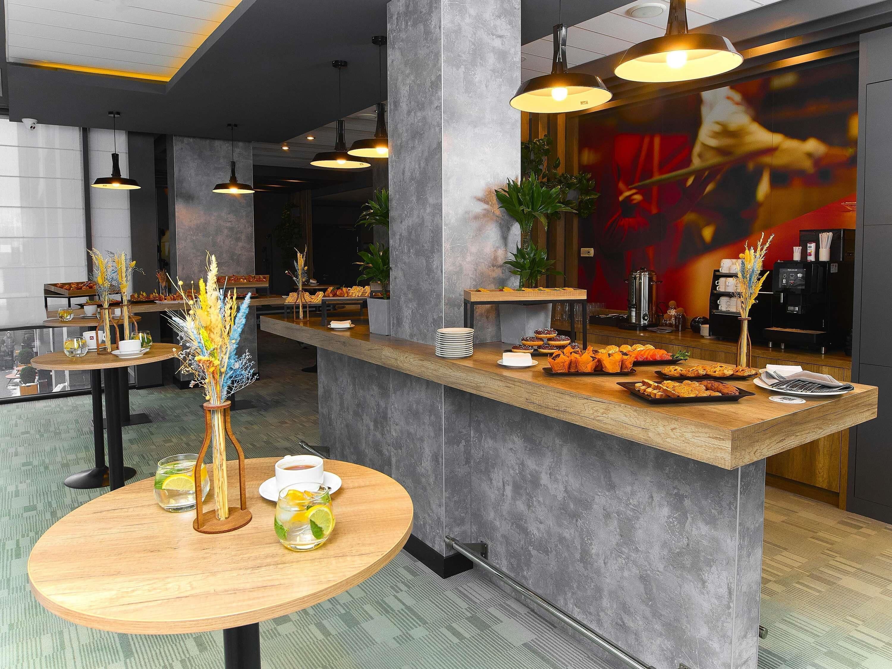 Een moderne hotellobby met een receptiebalie, zithoek en een koffieapparaat.