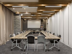 A conference room with a long table, chairs, a projector screen, and a poster on the wall. - ibis Kyiv Railway Station (Kyiv)