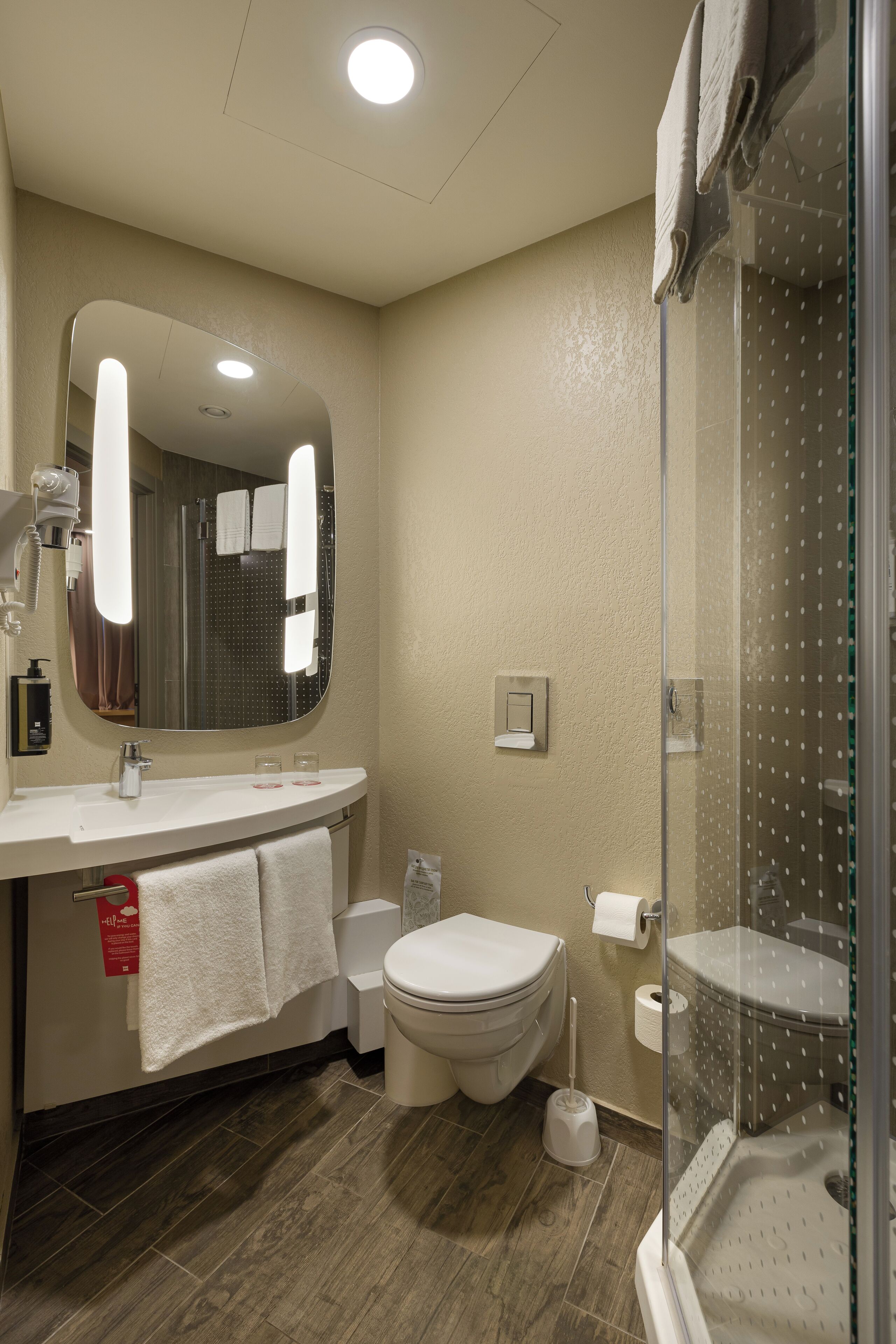 A modern bathroom with a large mirror, white sink, toilet, and a glass-enclosed shower.