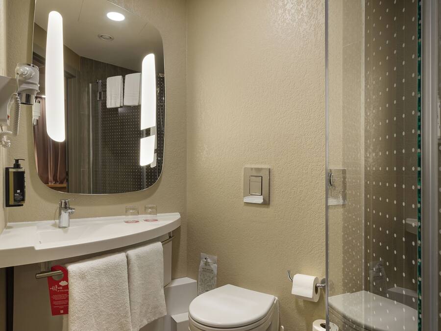 Un baño moderno con un espejo grande, lavamanos blanco, inodoro y ducha con mampara de vidrio.