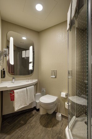 A modern bathroom with a large mirror, white sink, toilet, and a glass-enclosed shower. - ibis Kyiv Railway Station (Kyiv)