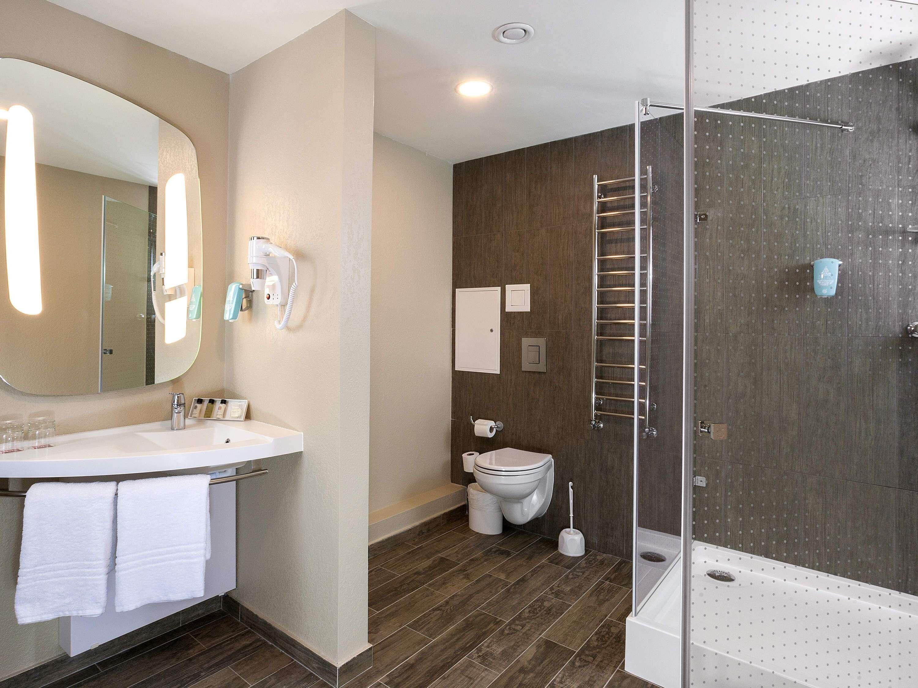 A modern bathroom with a large mirror, a sink, a toilet, and a shower area.