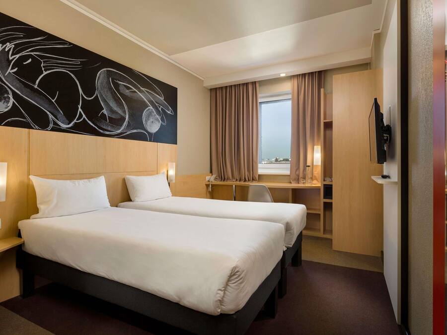 A hotel room with two beds, a desk, a TV, and a large abstract painting on the wall.