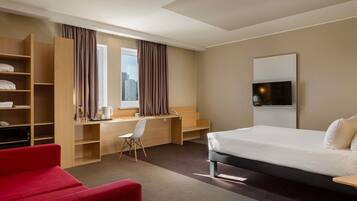 Habitación de hotel con cama, escritorio, silla, televisor y sofá rojo.