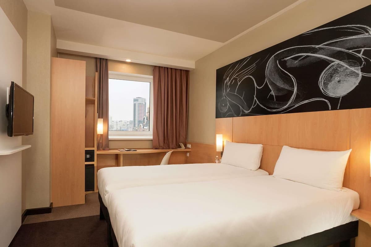 Hotellihuone, jossa on suuri sänky, työpöytä, tuoli, televisio ja näkymä kaupunkiin.