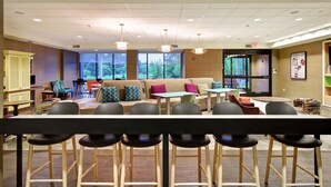 A modern lounge area with a sofa, chairs, and a bar with stools. - Home2 Suites by Hilton Mechanicsburg (Mechanicsburg)
