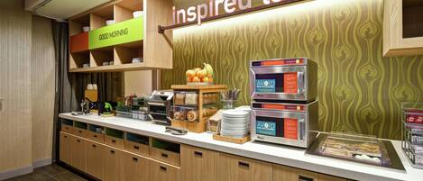 Un comptoir pour le petit-déjeuner avec une pancarte indiquant « table d’inspiration », une machine à café et un présentoir de fruits.