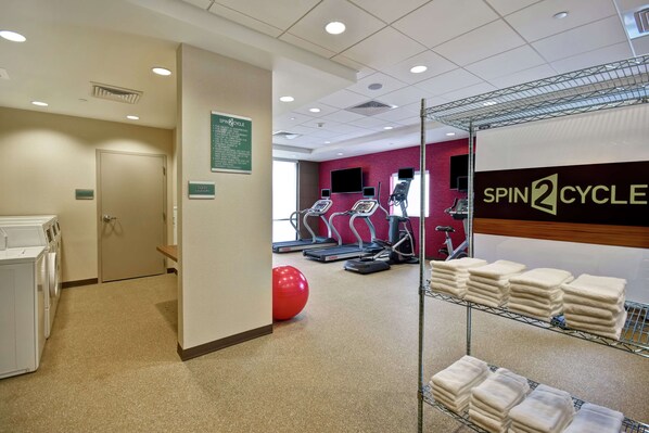 A gym with exercise equipment, a red exercise ball, and a wall-mounted sign reading "SPIN2CYCLE".