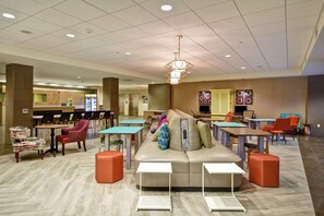 A modern lounge area with a central sofa, multiple tables, and chairs. - Home2 Suites by Hilton Mechanicsburg (Mechanicsburg)