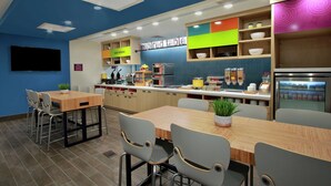 Un restaurante moderno con una pared azul de acento, un televisor de pantalla plana y diversas opciones de asientos, incluyendo mesas y sillas.