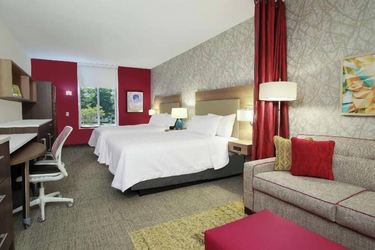 Habitación de hotel con una cama, dos mesitas de noche, un escritorio, una silla, un sofá y una ventana.