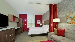 Una habitación de hotel con cama, sofá, televisión, escritorio y ventana.