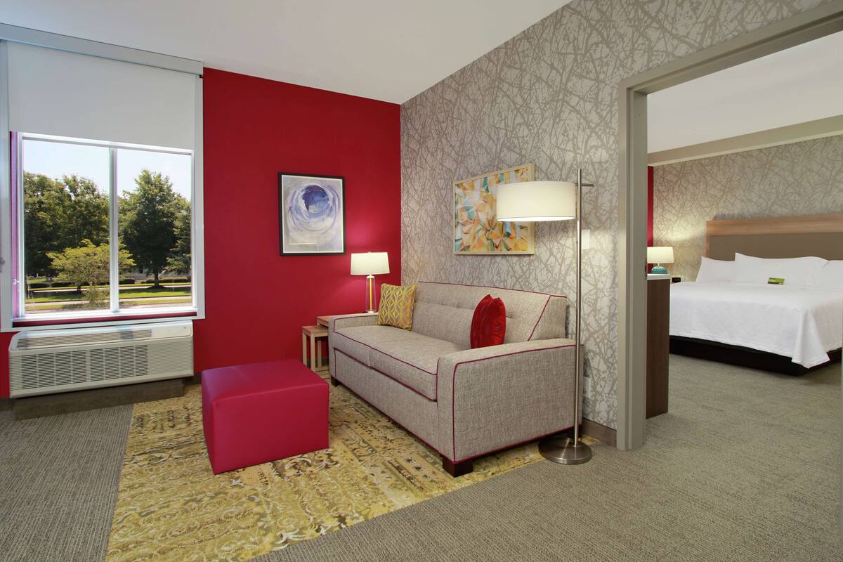 Camera d'albergo con una parete decorata in rosso, un divano, un letto, una finestra vista alberi e un tappeto a motivi.