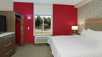 A hotel room with a bed, a TV, a wardrobe, a window with a view of trees, and a lamp.