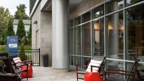 A hotel exterior with outdoor seating, a large glass window, and a sign for Hampton Inn Suites. - Hampton Inn & Suites Teaneck Glenpointe (Teaneck)