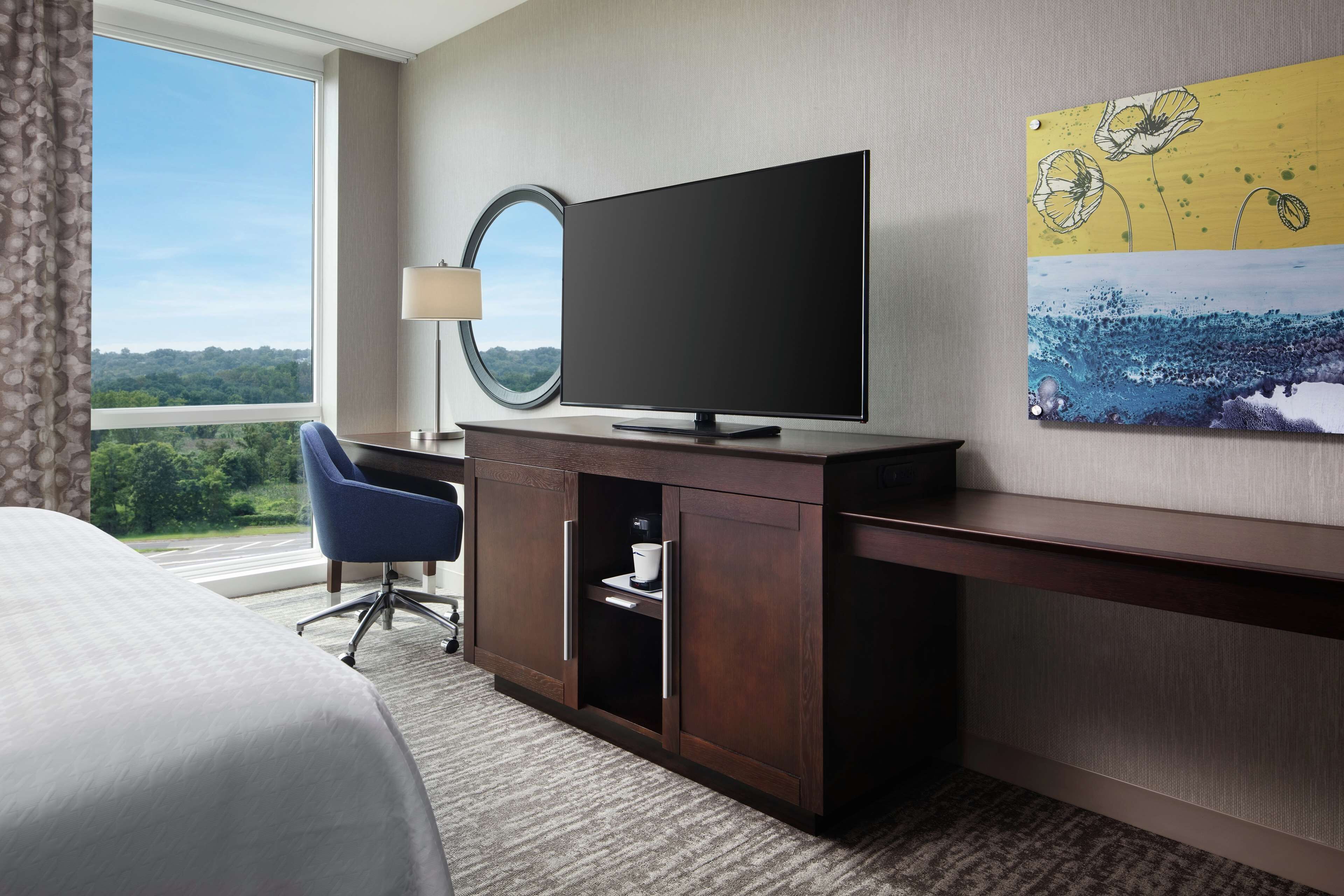 Een hotelkamer met een grote flatscreen-tv, een bureau met lamp, een blauwe stoel en een bed.