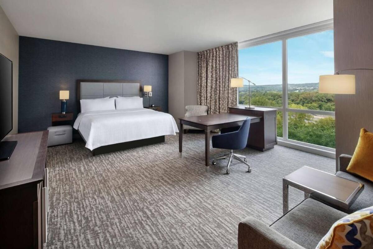 Une chambre d’hôtel équipée d’un lit, d’un bureau, d’une chaise et d’une grande fenêtre donnant sur un beau paysage.