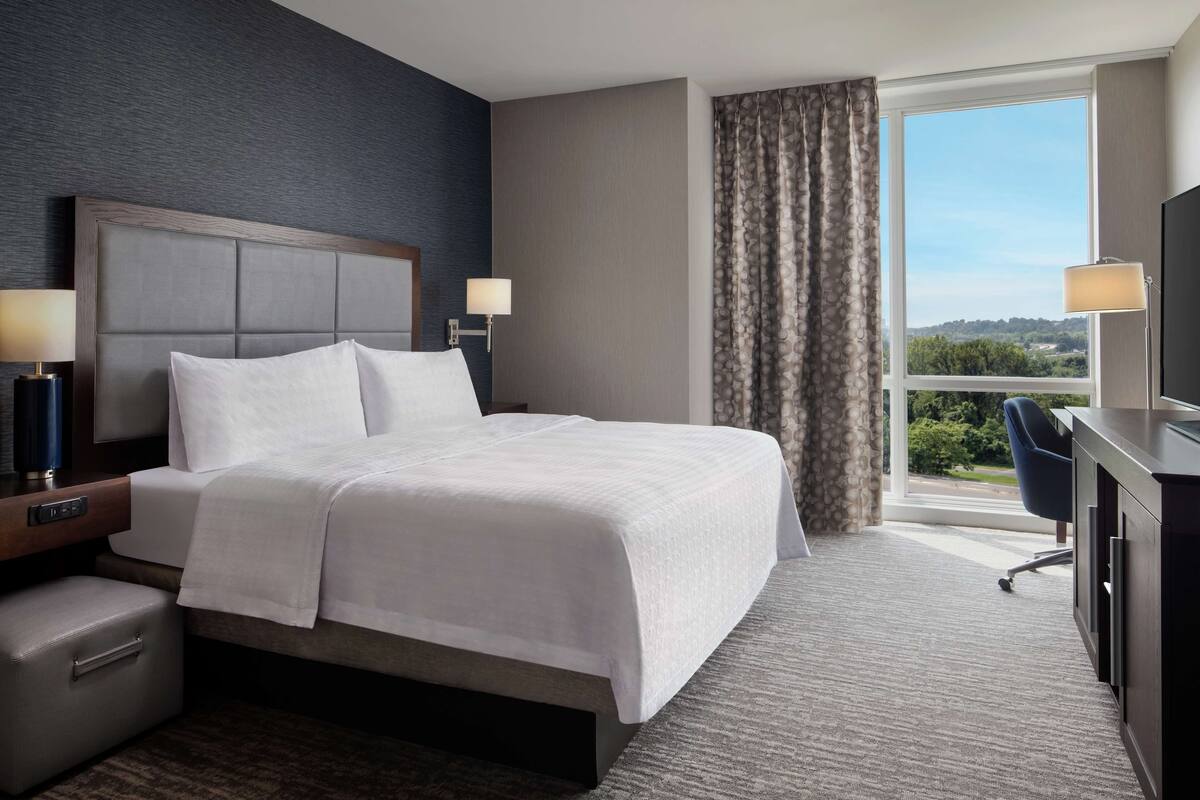 A hotel room with a large bed, a desk with a chair, a TV, and a window with curtains.