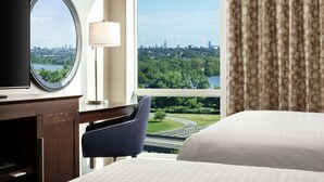 A hotel room with a large window offering a cityscape view, a bed, a desk with a television, and a chair. - Hampton Inn & Suites Teaneck Glenpointe (Teaneck)