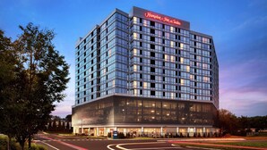 A modern hotel building with a large glass facade, a prominent signage at the top, and a well-lit entrance area. - Hampton Inn & Suites Teaneck Glenpointe (Teaneck)