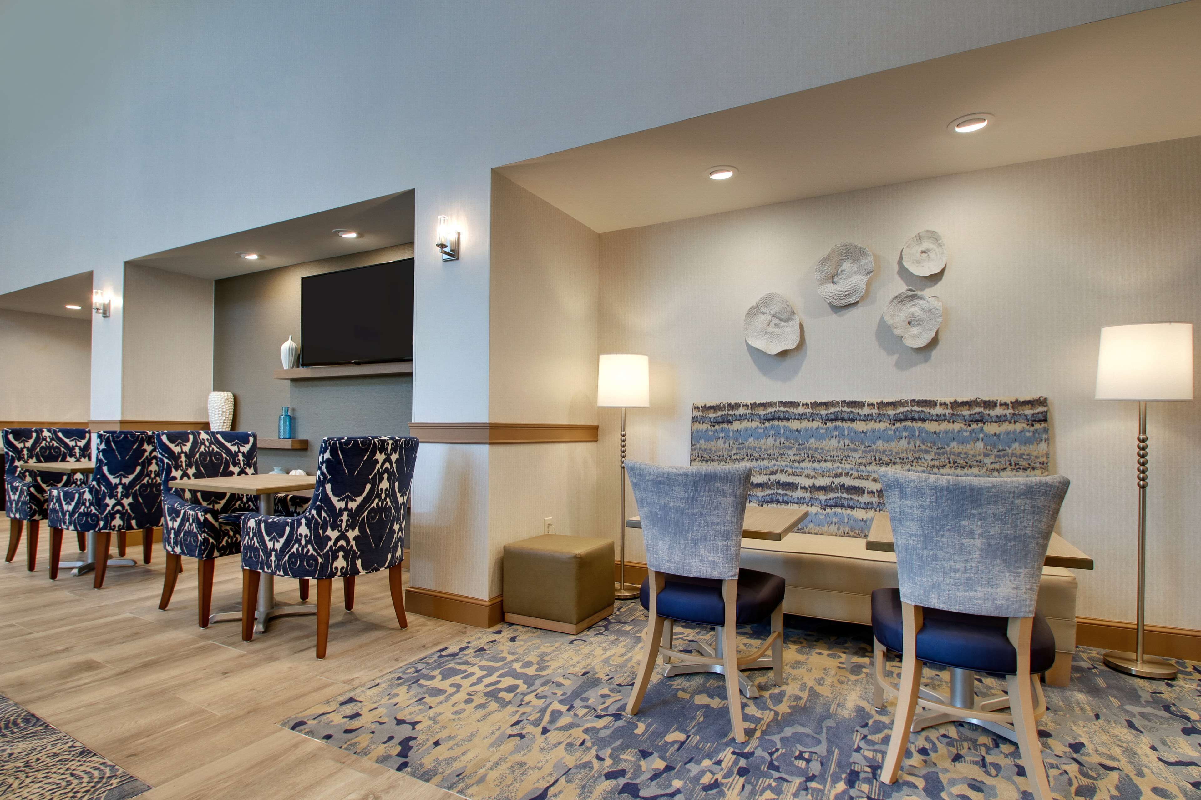 Een hotellobby met een zithoek met patroonstoelen en tafels, een wandgemonteerde flatscreen-tv en decoratieve wandkunst.
