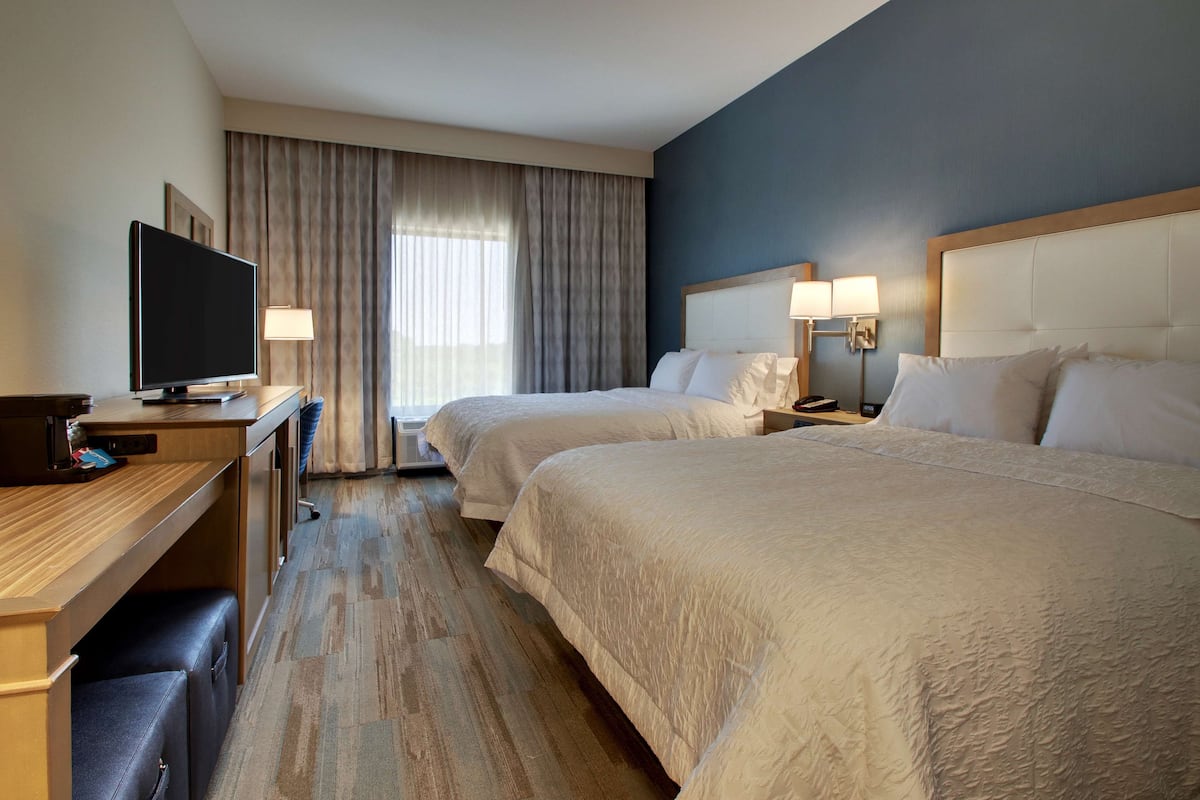 Habitación de hotel con dos camas, un escritorio, un televisor y una ventana con cortinas.