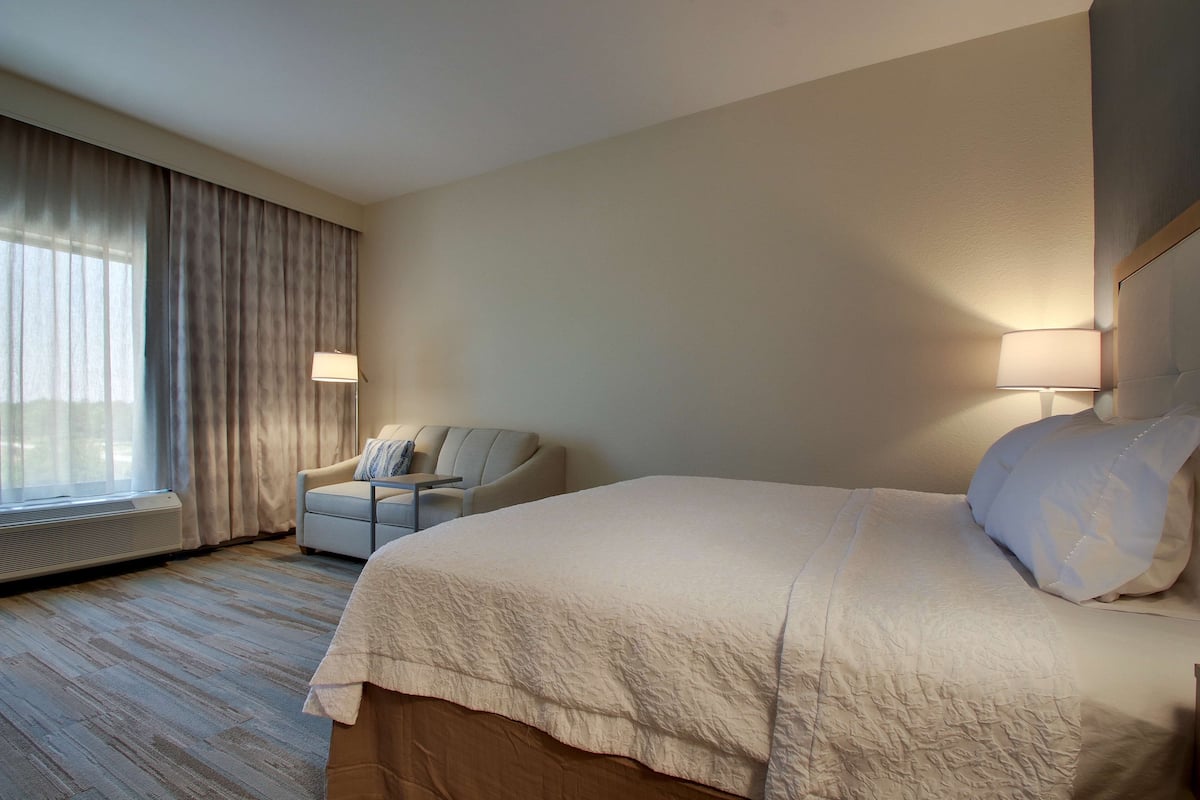 Una habitación de hotel con una cama grande, una silla, un escritorio y una ventana con cortinas.