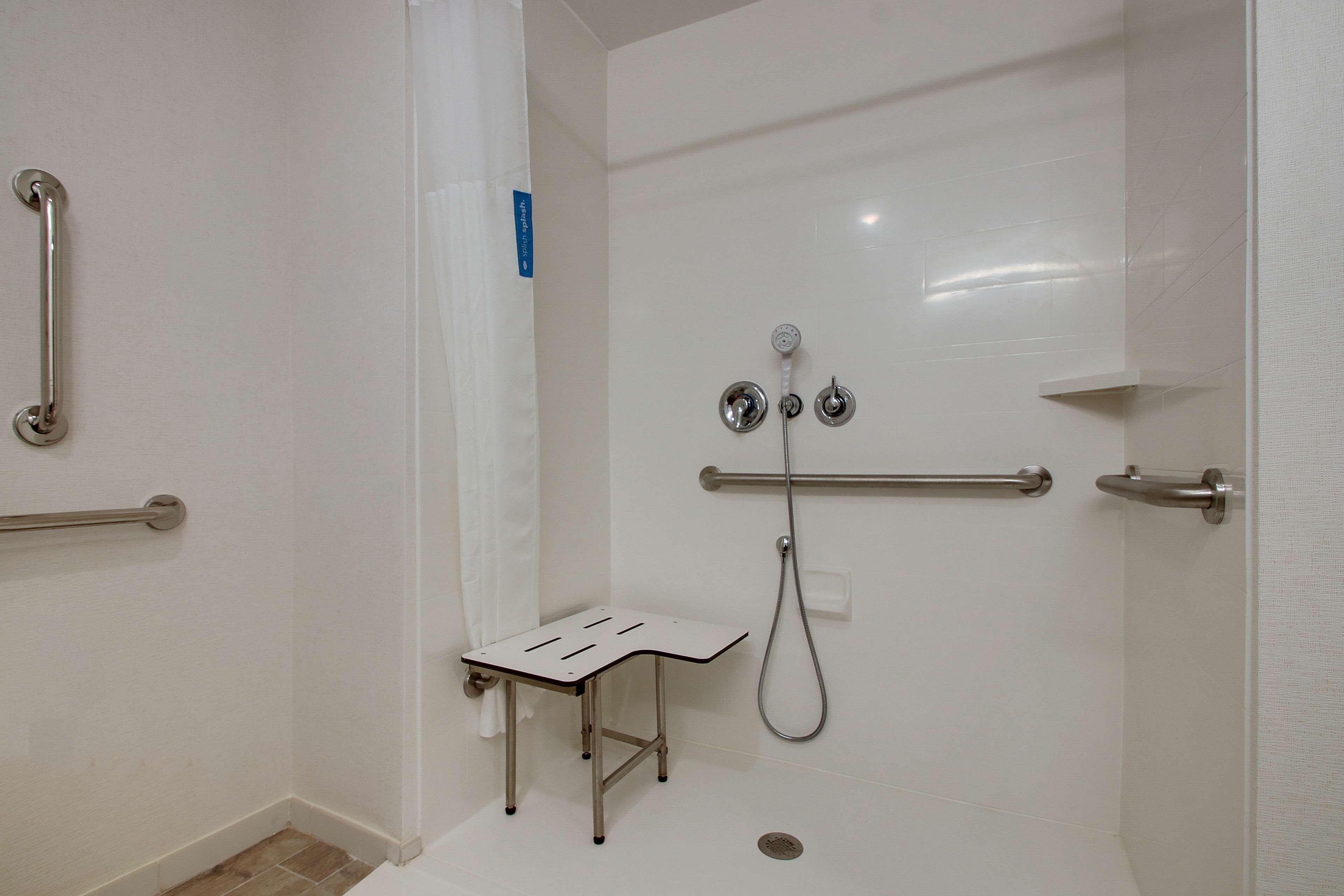 Un baño con ducha, barras de apoyo y un taburete pequeño.