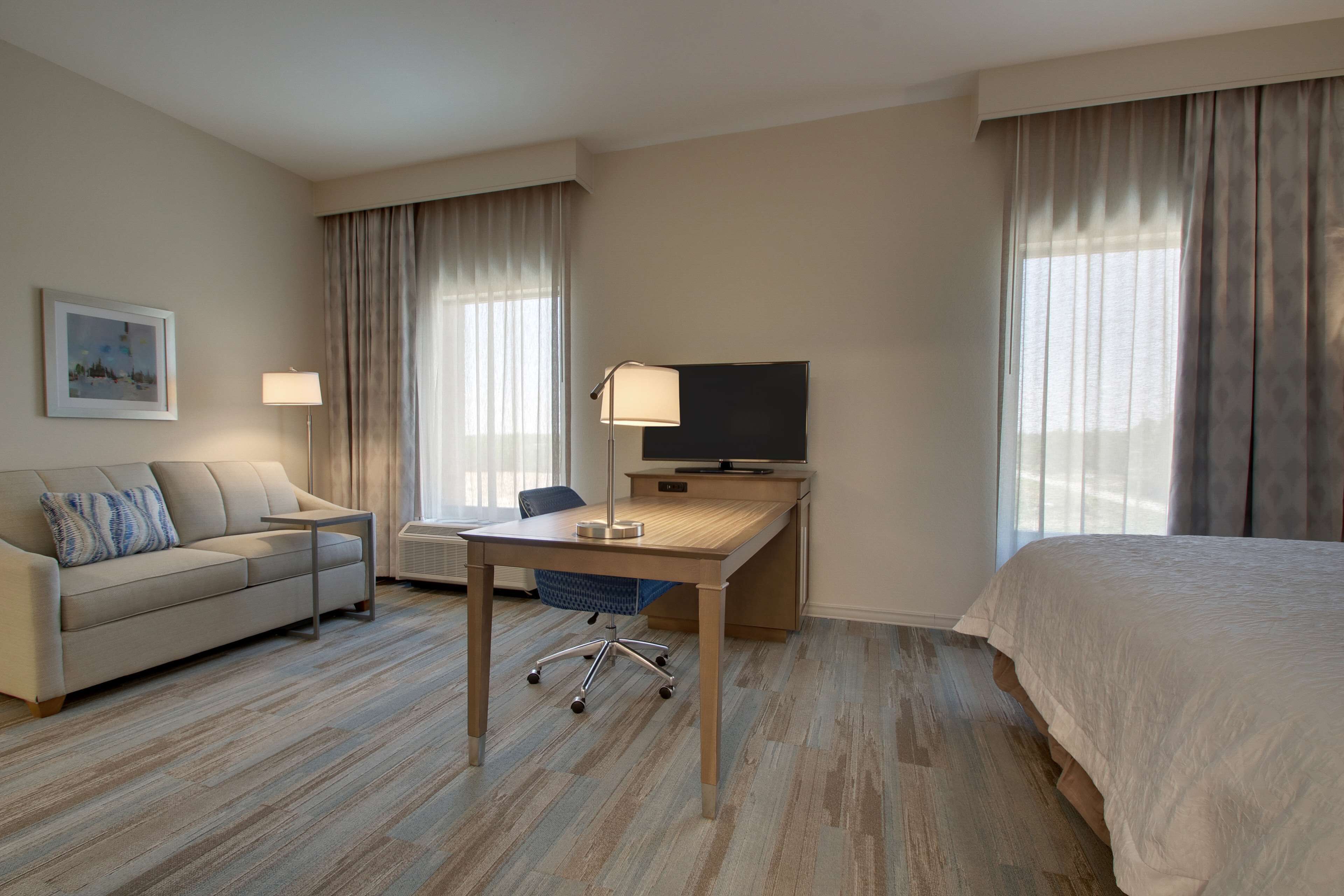 Une chambre d’hôtel comprenant un lit, un bureau avec une chaise, une télévision, un canapé et une fenêtre avec des rideaux.