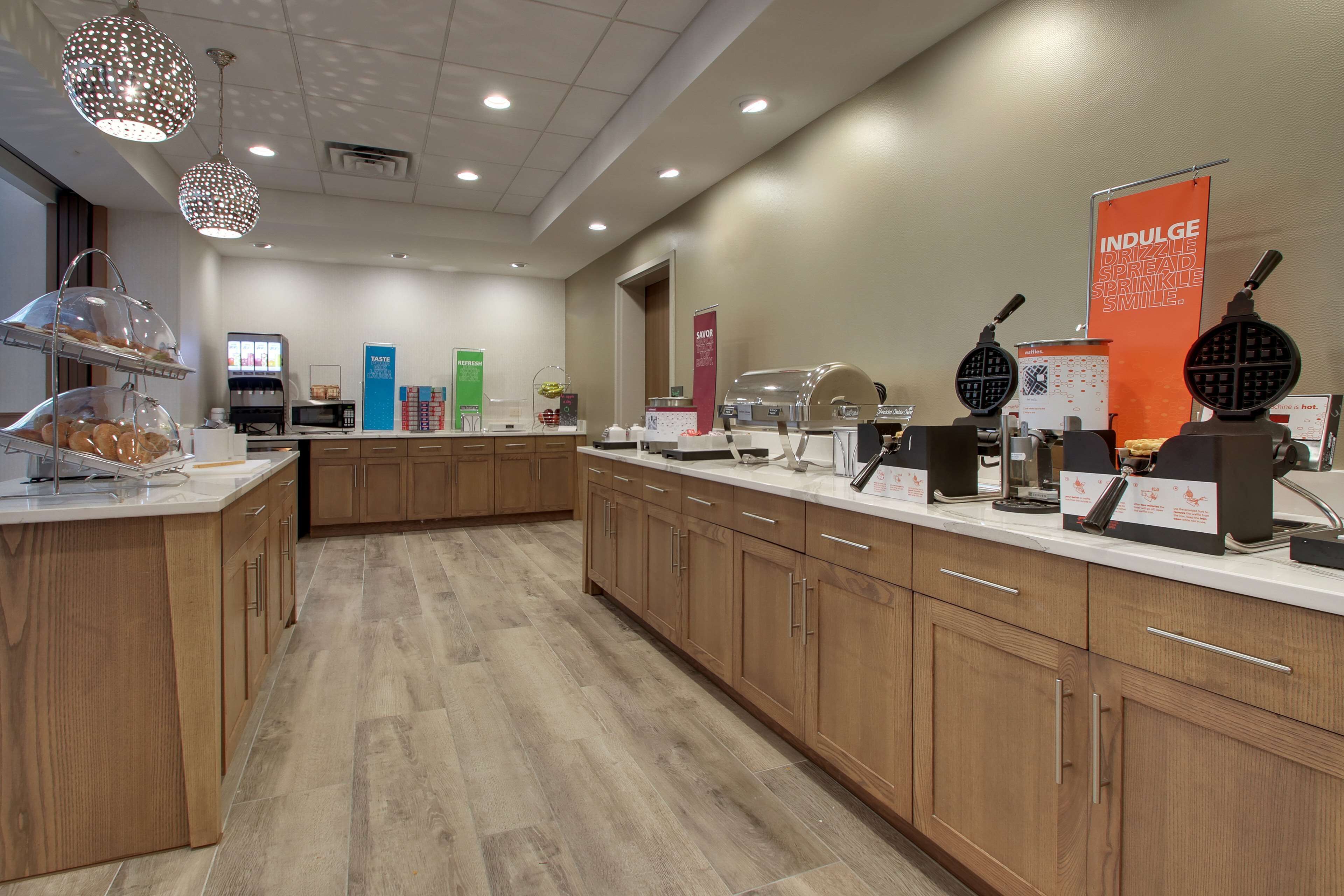 Un'area cucina moderna con isola centrale, mobili in legno e diversi elettrodomestici tra cui una macchina per il caffè e un waffle maker.