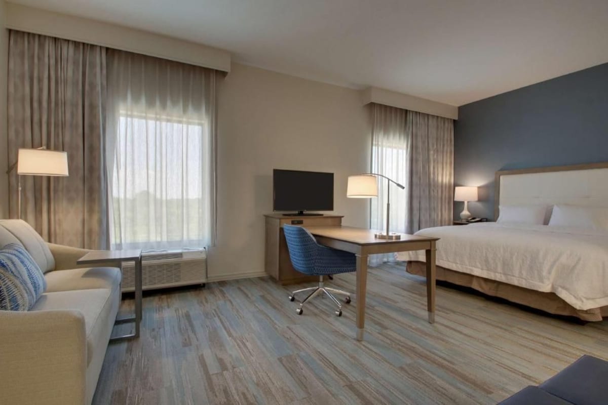 A hotel room with a bed, a desk with a chair, a television, and a lamp.