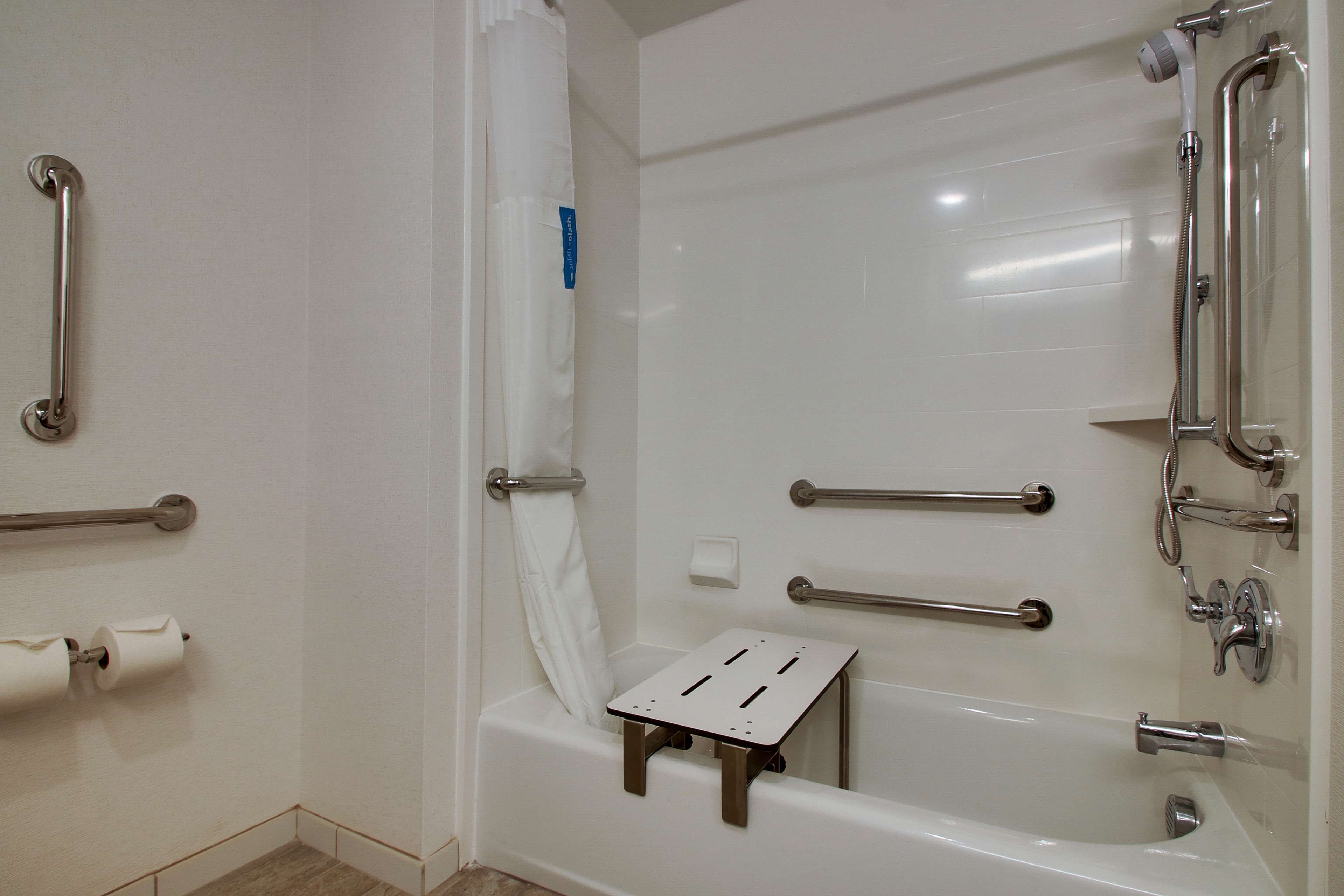 Une salle de bain équipée d’une baignoire, de barres d’appui, d’un pommeau de douche et d’un porte-rouleau de papier toilette.
