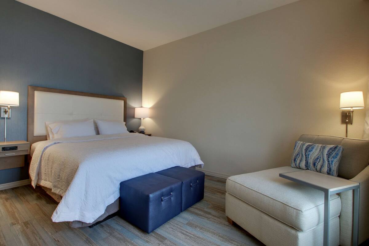 Una habitación de hotel con cama, mesitas de noche, una silla y un banco.