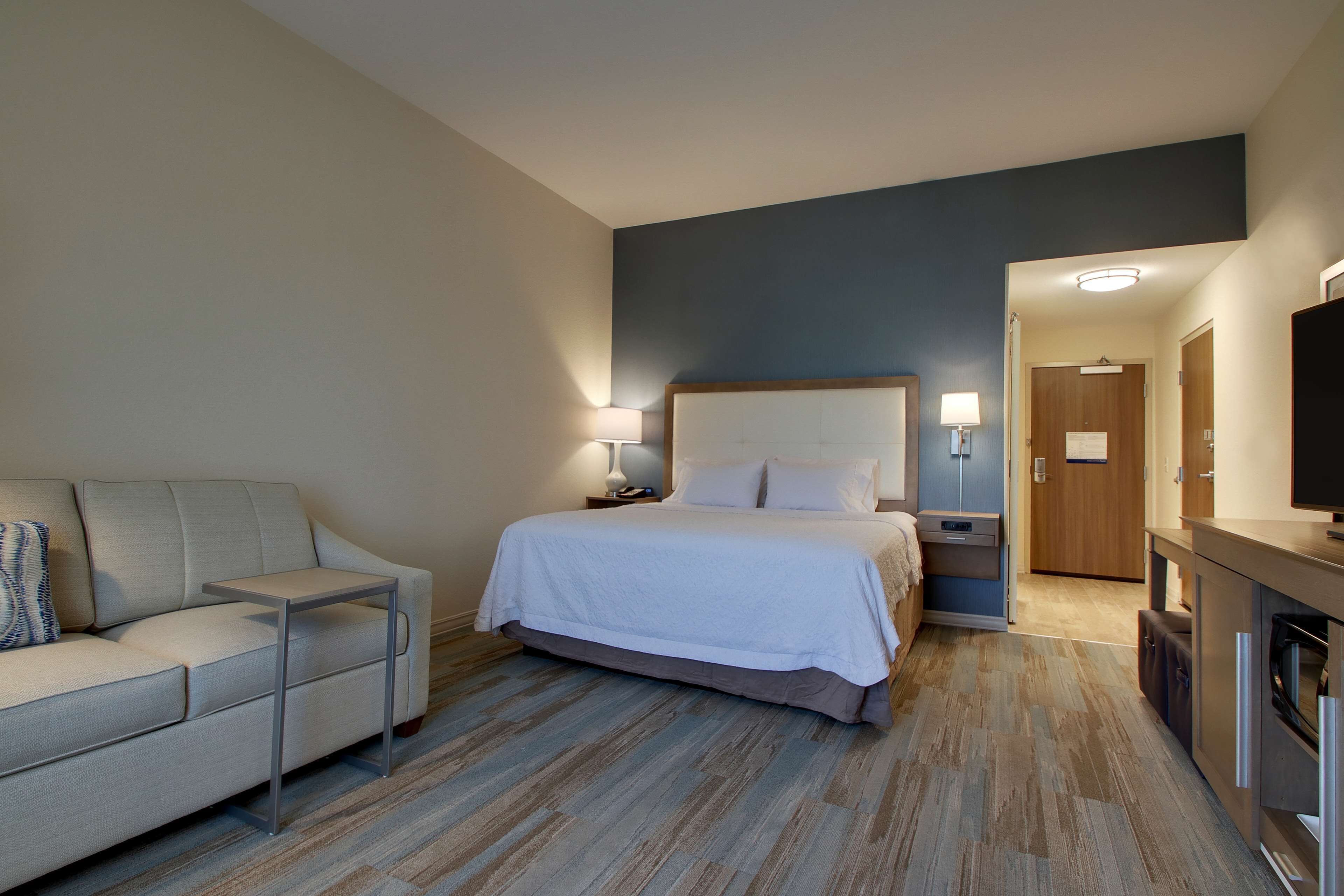 Une chambre d’hôtel avec un lit, un canapé, une télévision, un bureau et un plancher en bois.