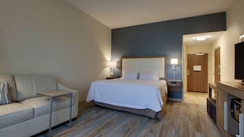 Une chambre d’hôtel avec un lit, un canapé, une télévision, un bureau et un plancher en bois.