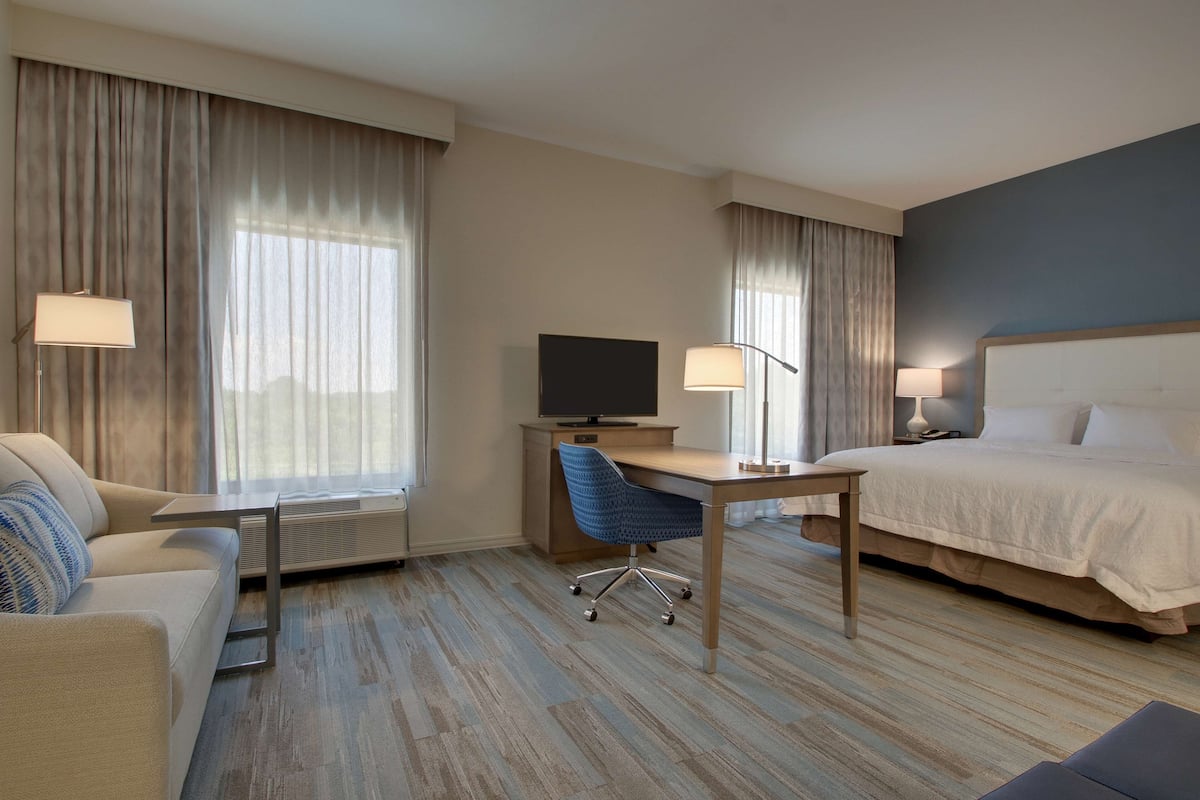 Habitación de hotel con cama, escritorio, silla, televisor y ventana con cortinas.