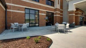 A brick building with a patio area featuring outdoor seating and a small garden bed. - Hampton Inn Sneads Ferry North Topsail Beach (Sneads Ferry)