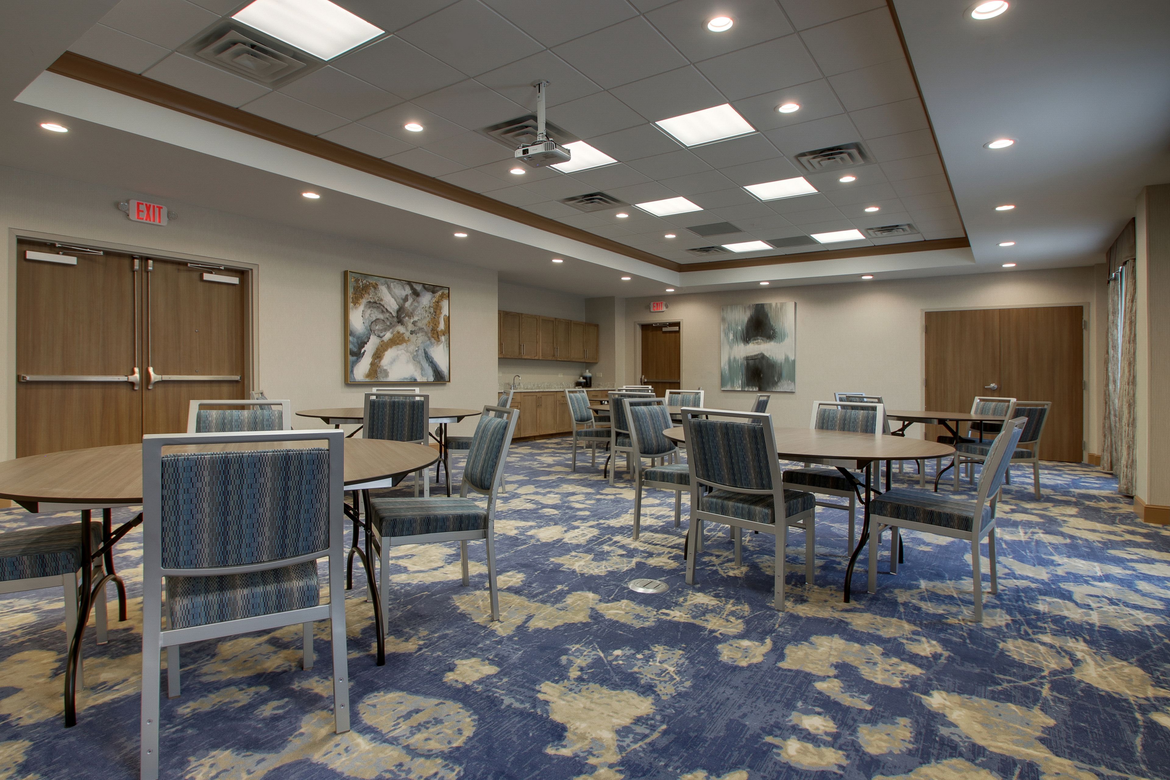 A conference room with tables and chairs, a carpeted floor, and a ceiling with recessed lighting.