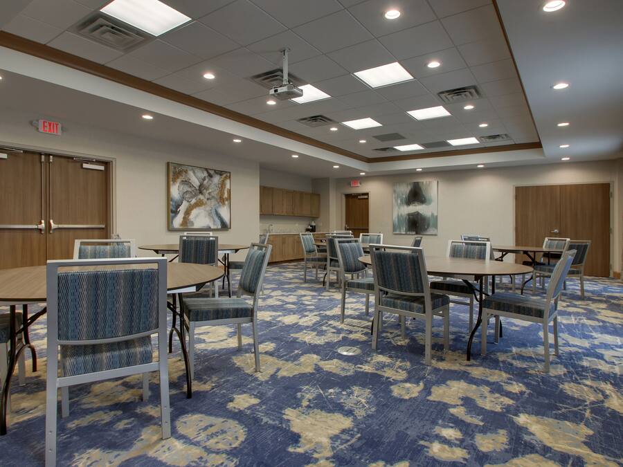 A conference room with tables and chairs, a carpeted floor, and a ceiling with recessed lighting.