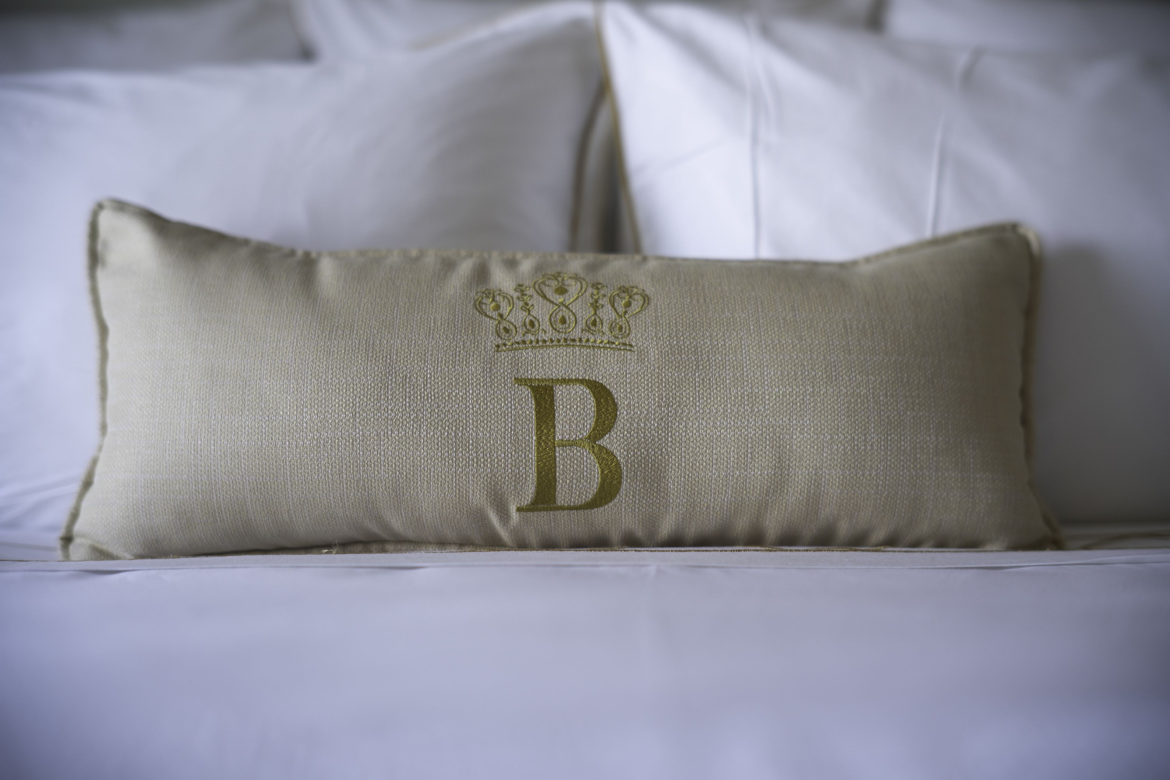 A bed with a single pillow featuring a monogram and a crown embroidery.