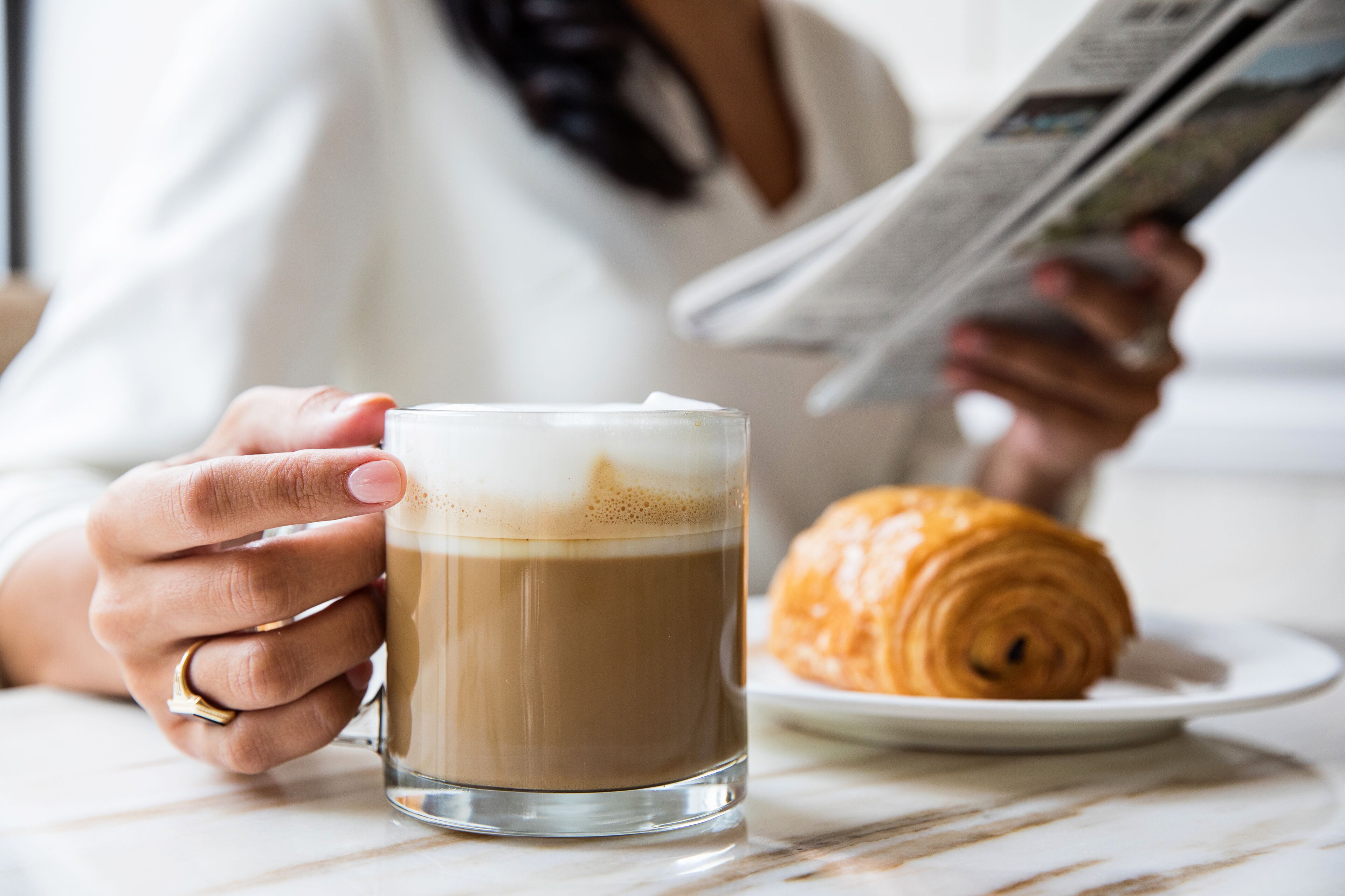 Eine Person hält eine Kaffeetasse, auf einem Teller liegt ein Croissant.