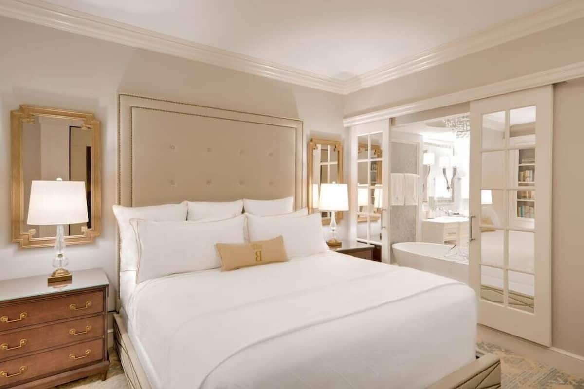 A spacious bedroom with a large bed, a nightstand with a lamp, and a wardrobe with a mirror.