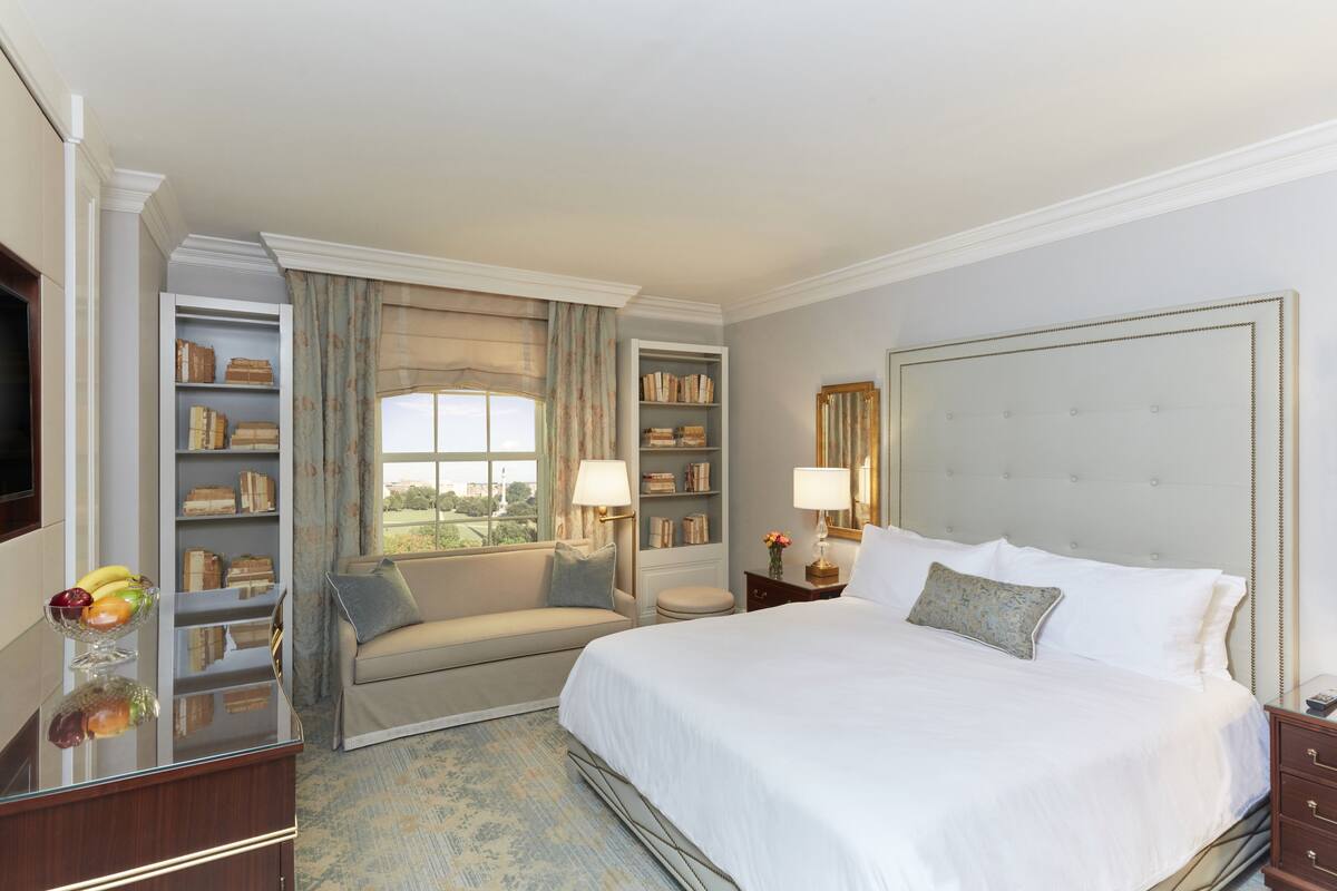 Quarto de hotel com uma cama grande, um sofá, uma mesinha com uma cesta de frutas e estantes embutidas.
