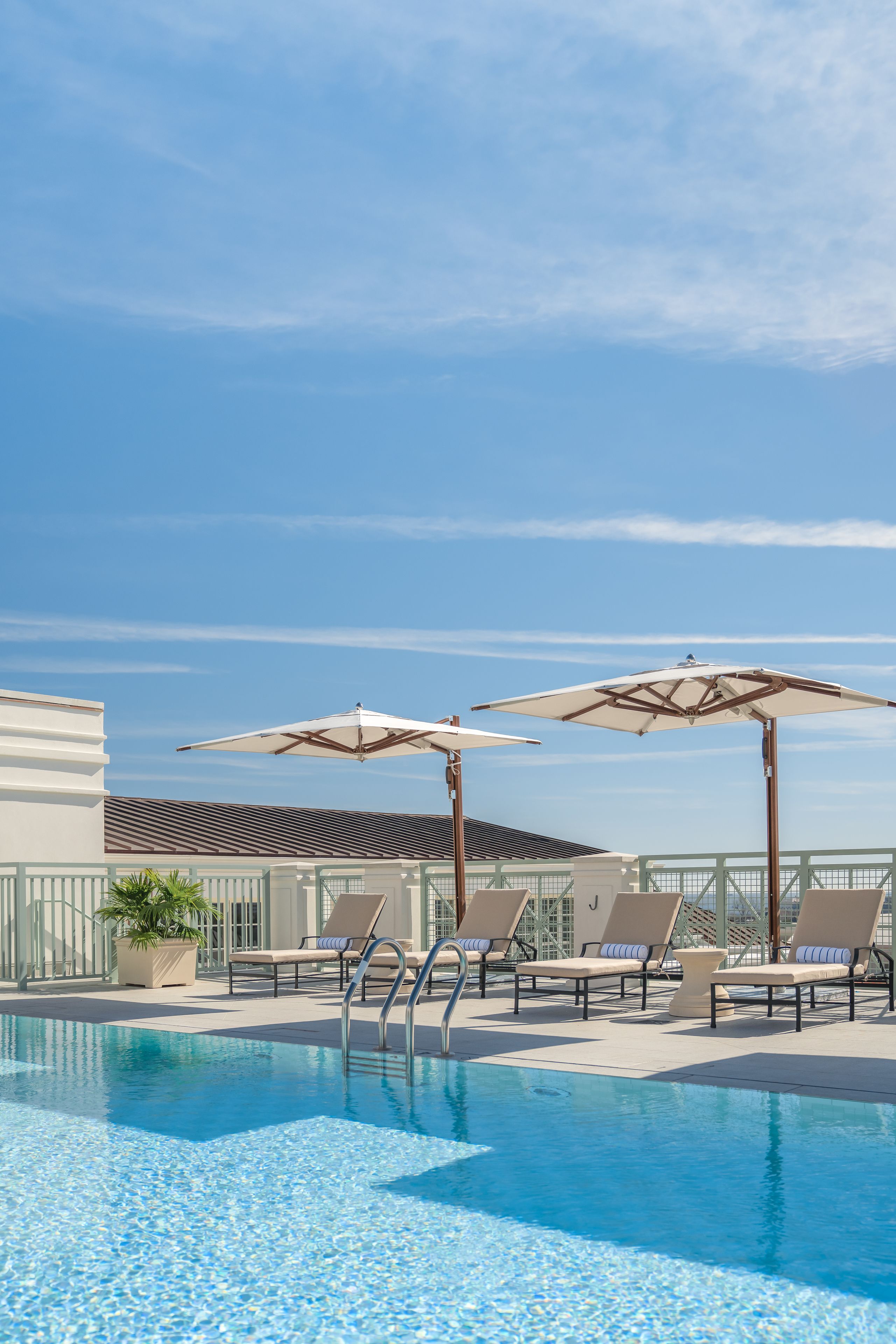 A pool area with lounge chairs and umbrellas, a clear sky, and a building in the background.