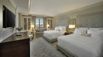 A hotel room with two beds, a TV, a desk, and a view of the city.