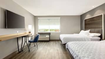 A modern hotel room with a desk, two beds, a large window, and a flat-screen TV.