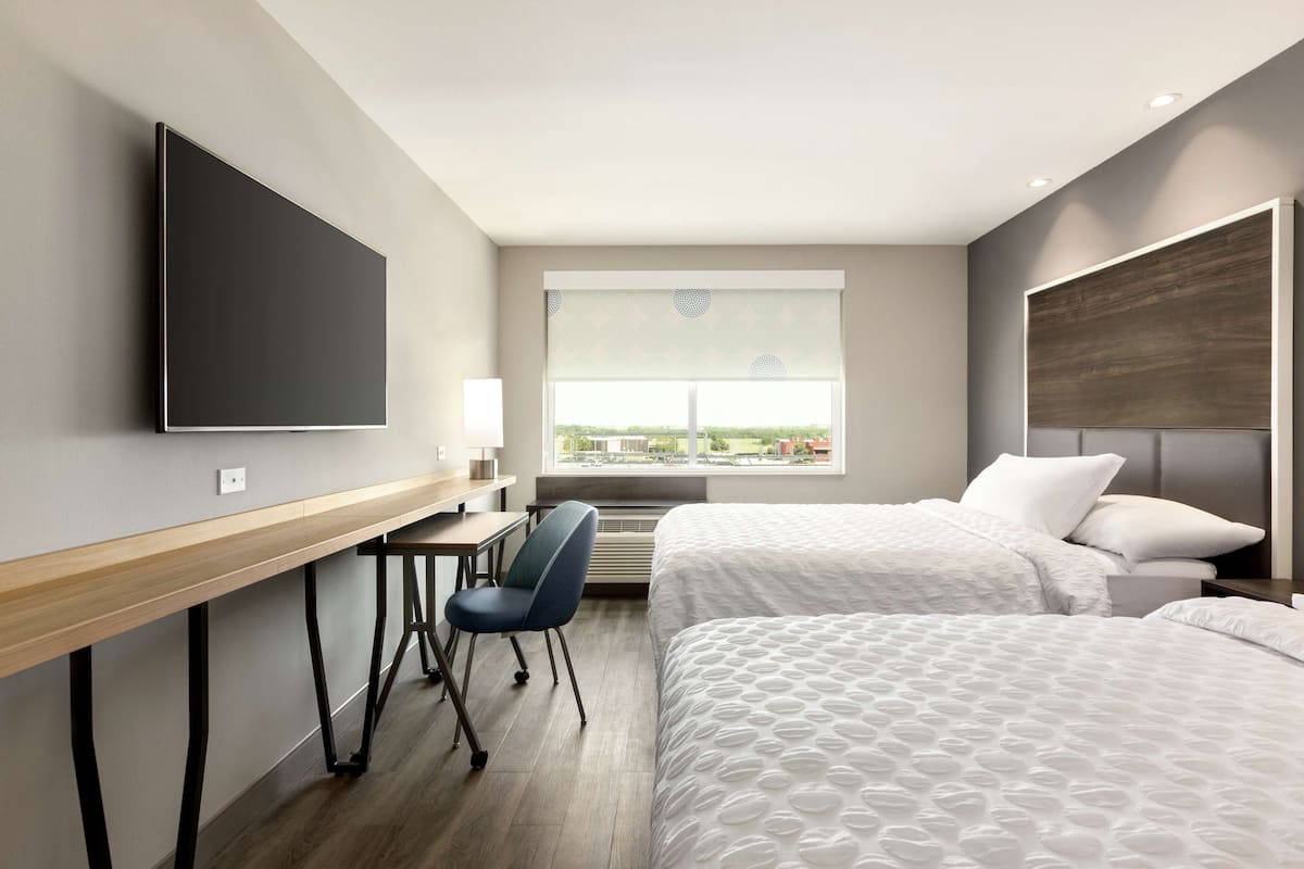 A hotel room with a bed, a desk, a chair, a TV, and a window with a view.